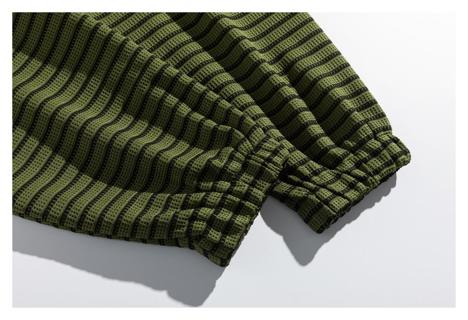 Close-up of a gathered sleeve cuff on an olive-green and black striped garment.