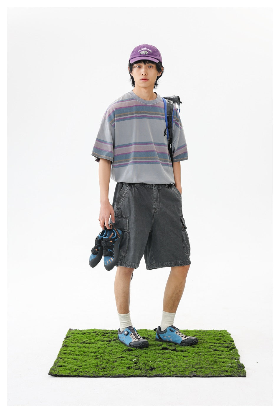 Front view of a model wearing a loose gray T-shirt with muted purple, blue, and tan stripes.
