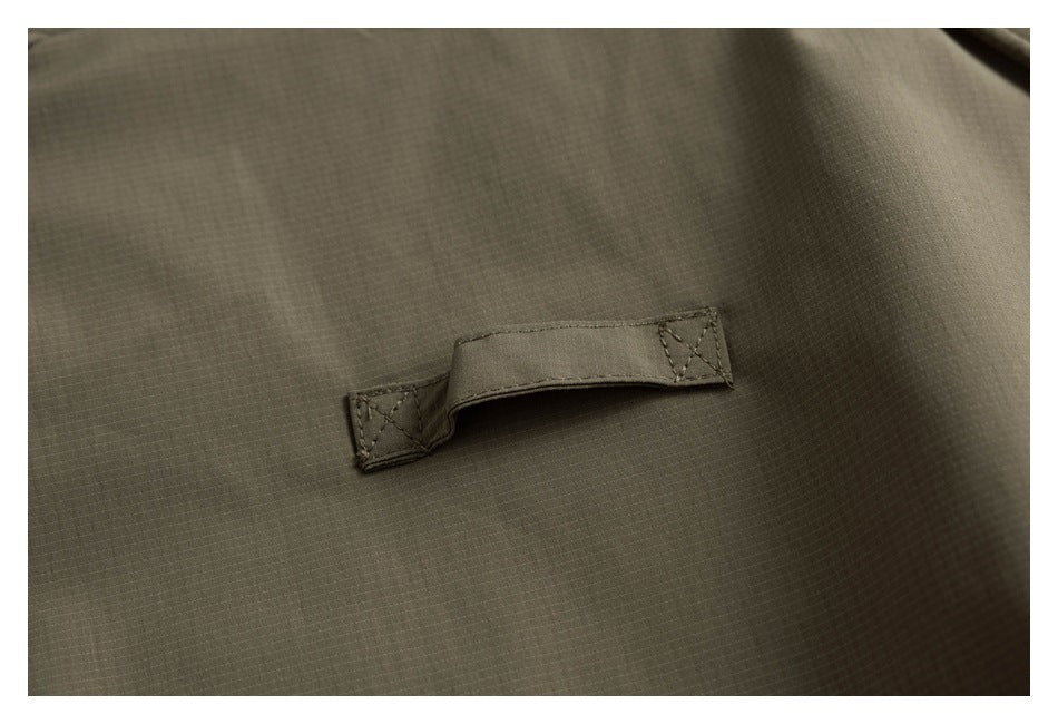 Close-up of a stitched fabric tab on olive-green ripstop garment fabric.