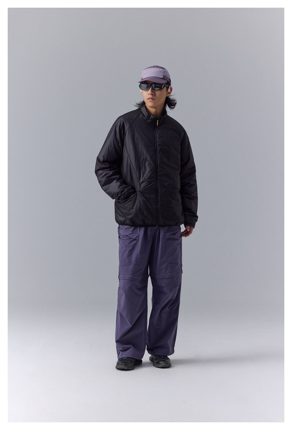 Front view of a model in a black zip-front jacket and purple cargo pants.