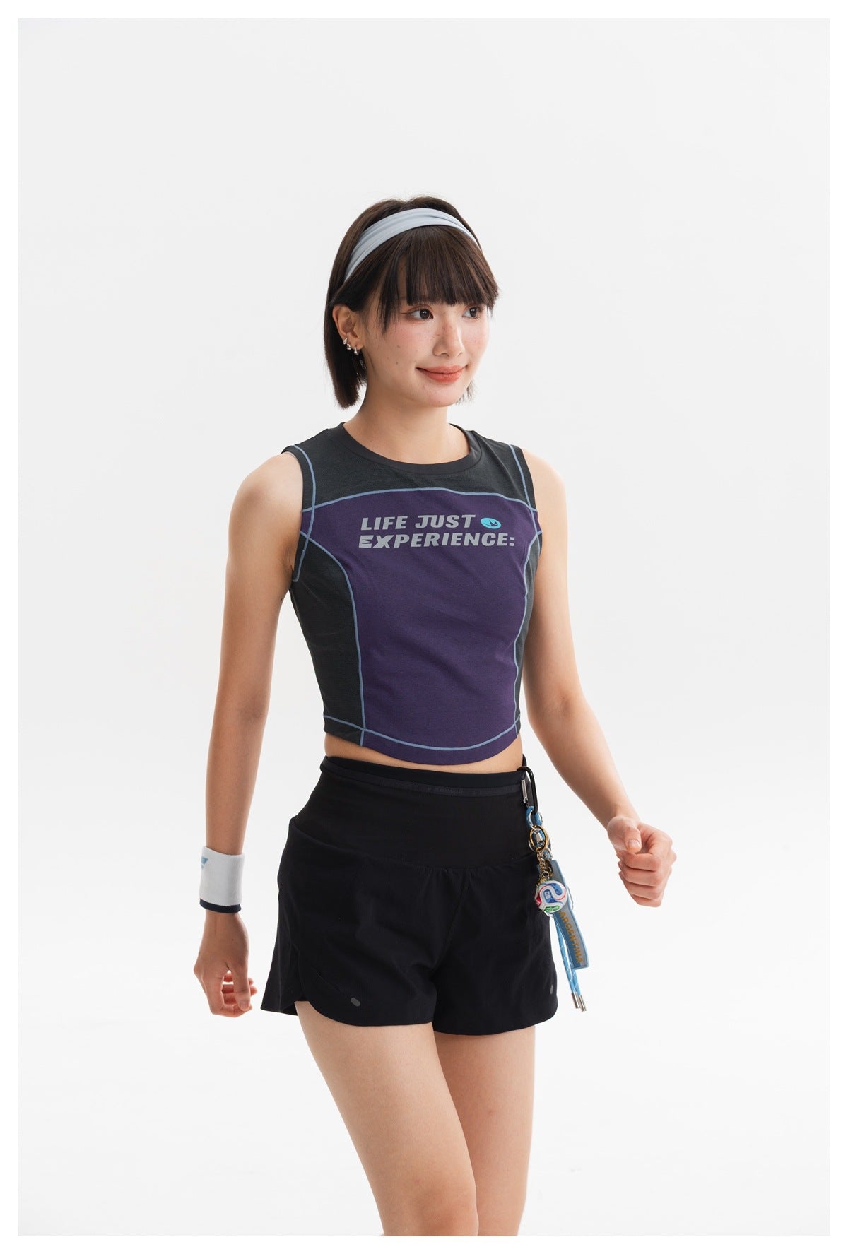 Model wearing a purple and charcoal sleeveless crop top with blue piping and black shorts.