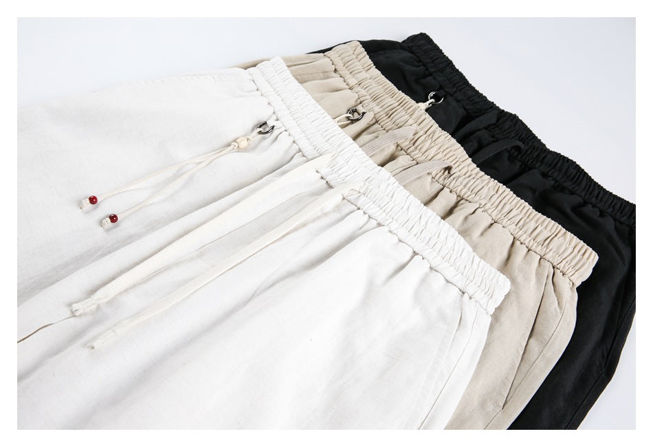 White, beige, and black pants arranged together, showing elastic waistbands, drawstrings, and pockets.