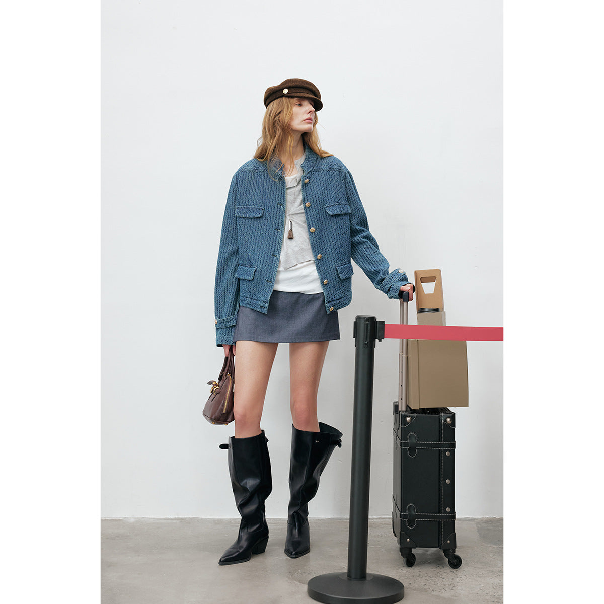 Model wearing a textured blue jacket with gold buttons and flap pockets, a gray mini skirt, and black knee-high boots.