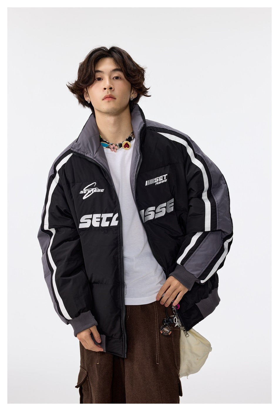 Model wearing an open black quilted jacket with gray sleeves and white stripes over a white tee and brown pants