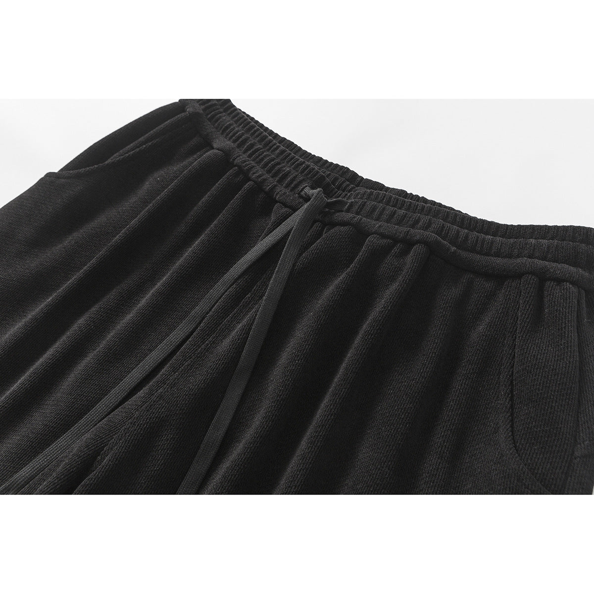 Close-up of black pants showing the elastic drawstring waistband and gathered front.