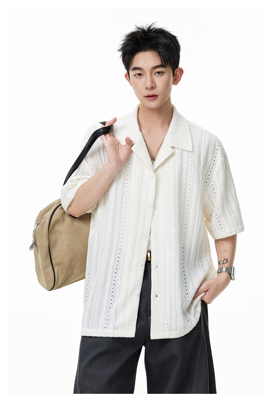 Model wearing an ivory short-sleeve openwork button-up shirt, carrying a tan shoulder bag.
