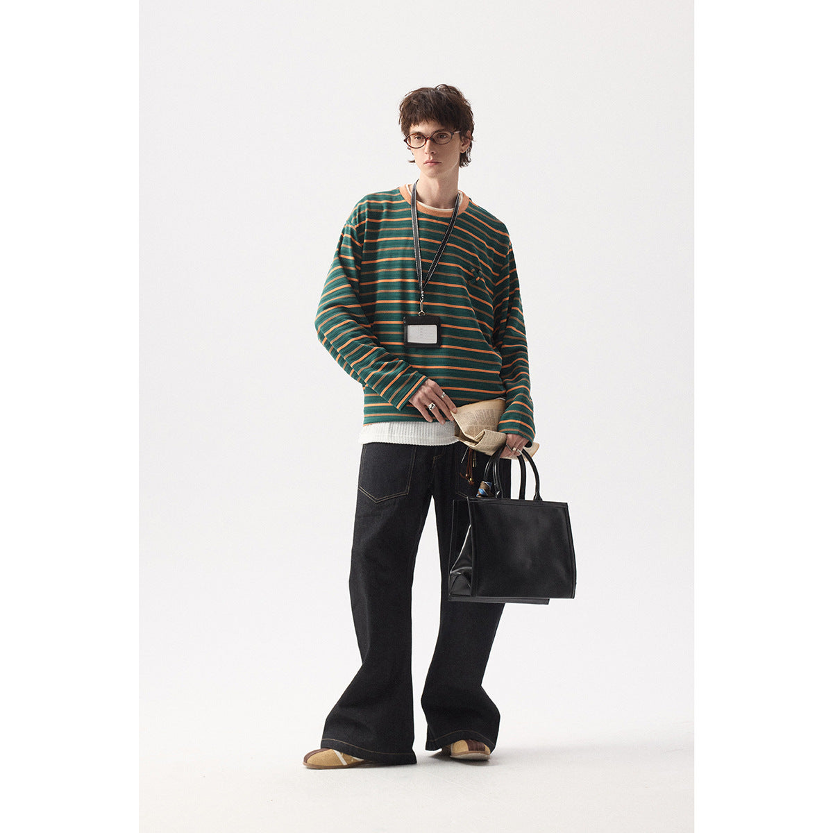 Full-length view of a model wearing a green and orange striped shirt with black wide-leg jeans.