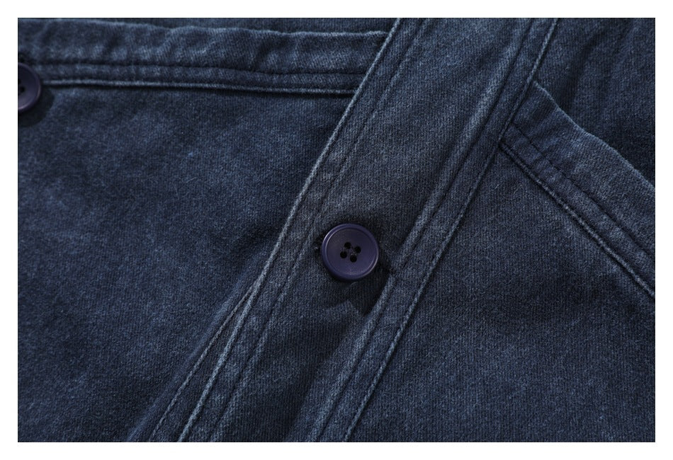 Close-up of dark indigo fabric with a button, stitched seams and a diagonal overlapping panel.