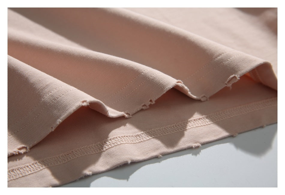 Close-up of light blush-pink garment fabric showing stitched hems and a slightly frayed edge.