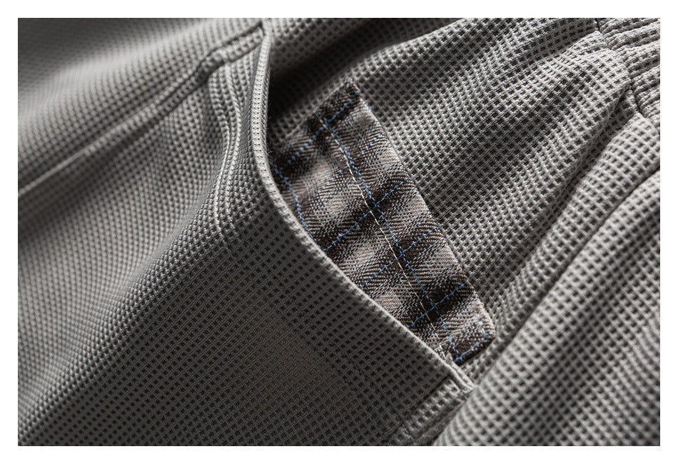 Close-up of a pocket opening with brown plaid trim on gray textured shorts.