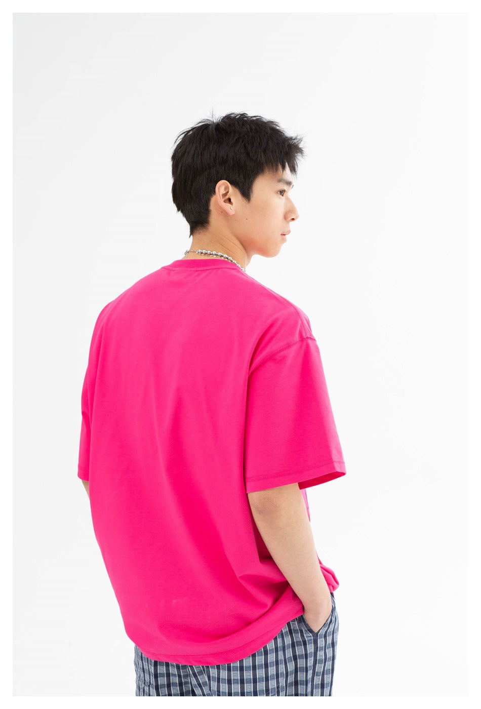 A person wearing an oversized bright pink T-shirt, shown from the back with blue plaid shorts.