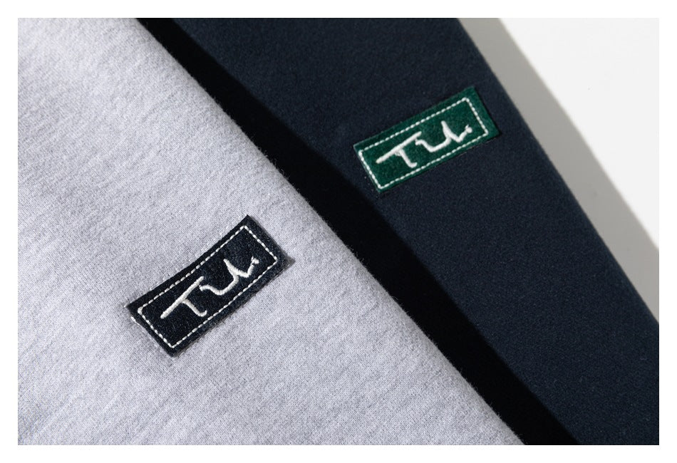 Close-up of embroidered rectangular logo patches on light gray and navy sweatshirt fabric.