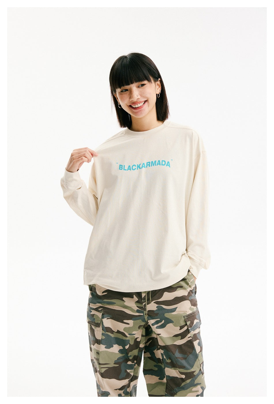 Model displaying the turquoise chest lettering on an ivory long-sleeve shirt with camouflage cargo pants.