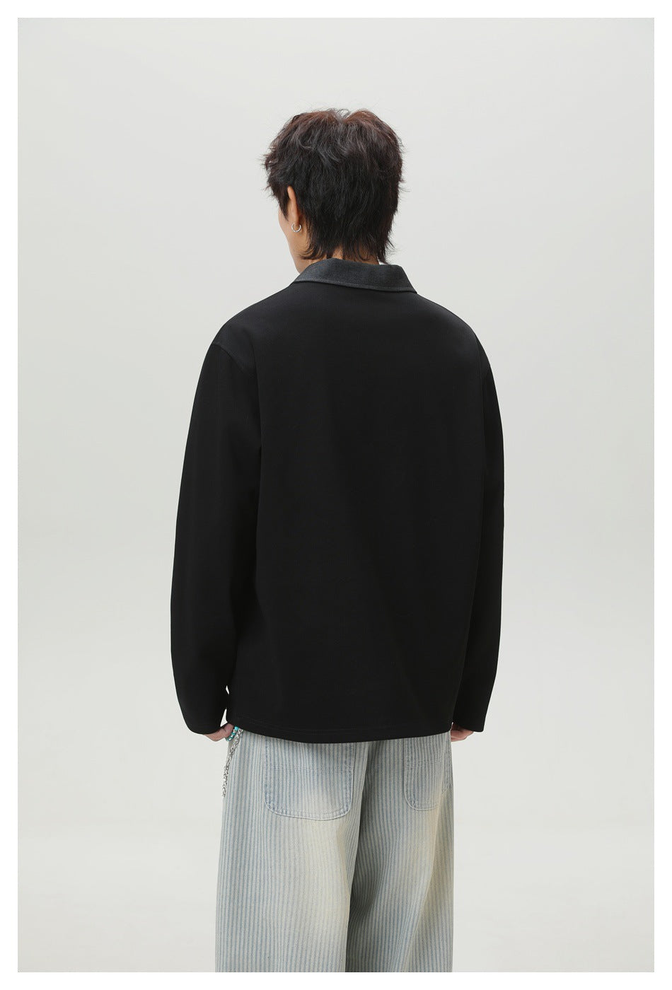 Back view of a model wearing a black long-sleeve top with a charcoal collar and pale striped pants.