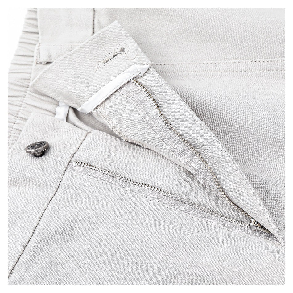 Close-up of the light gray trousers' open zipper fly and metal button.