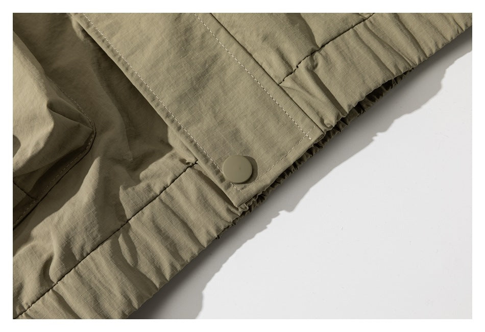 Close-up of a khaki jacket hem with a snap-fastened tab and gathered elastic edge.