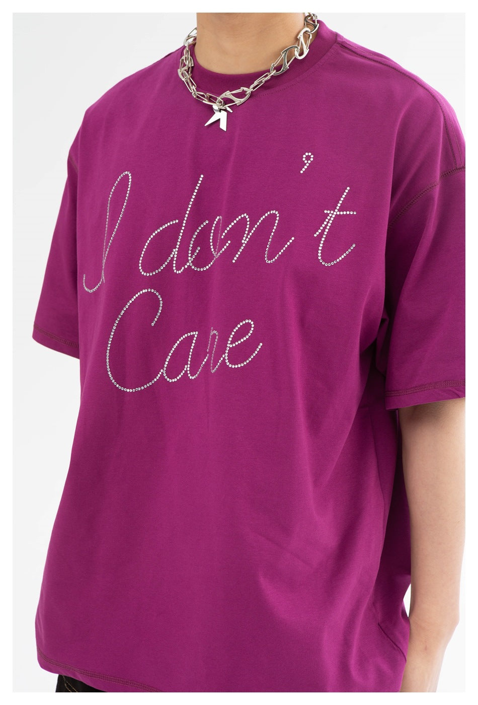 Close view of a model wearing a magenta T-shirt with rhinestone “I don't Care” script and a silver chain necklace.