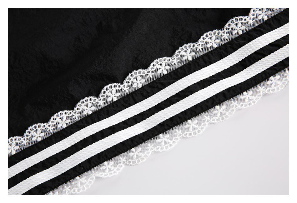 Close-up of two white stripes and floral lace trim on black pants.