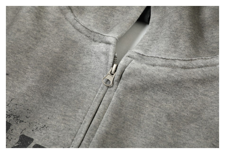 Close-up of a silver zipper and seams on a heather gray garment, with part of a dark print at the edge.