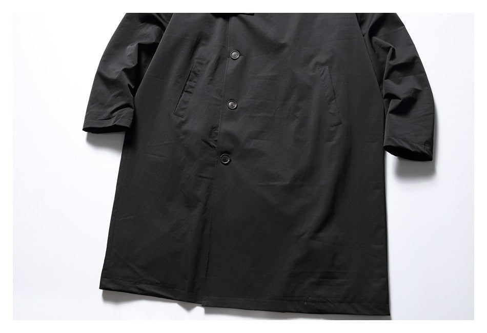 Front view of the black coat’s buttoned body, slanted pockets, long sleeves, and lower hem.