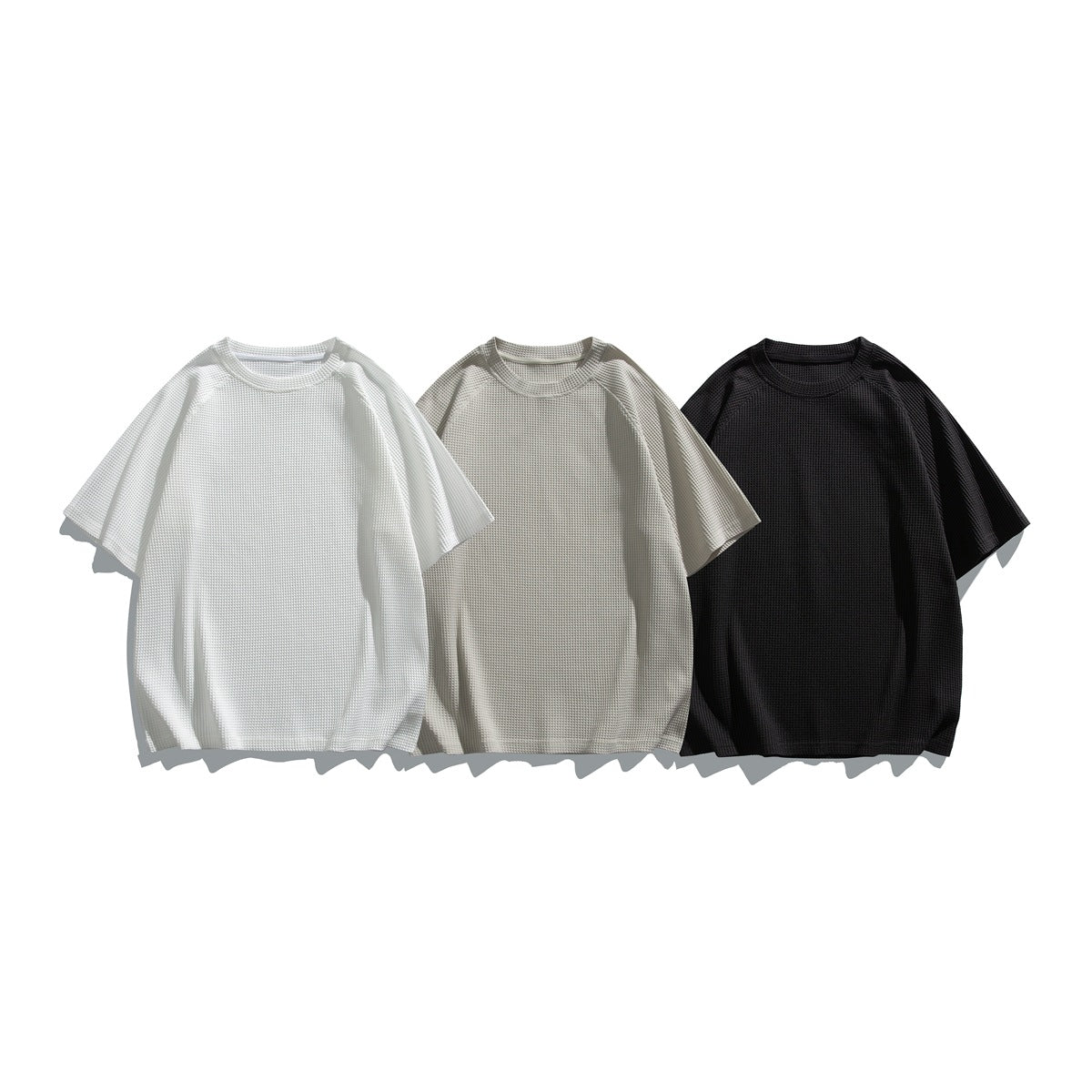 Three short-sleeve crew-neck waffle-textured shirts shown from the front in white, light beige, and black.