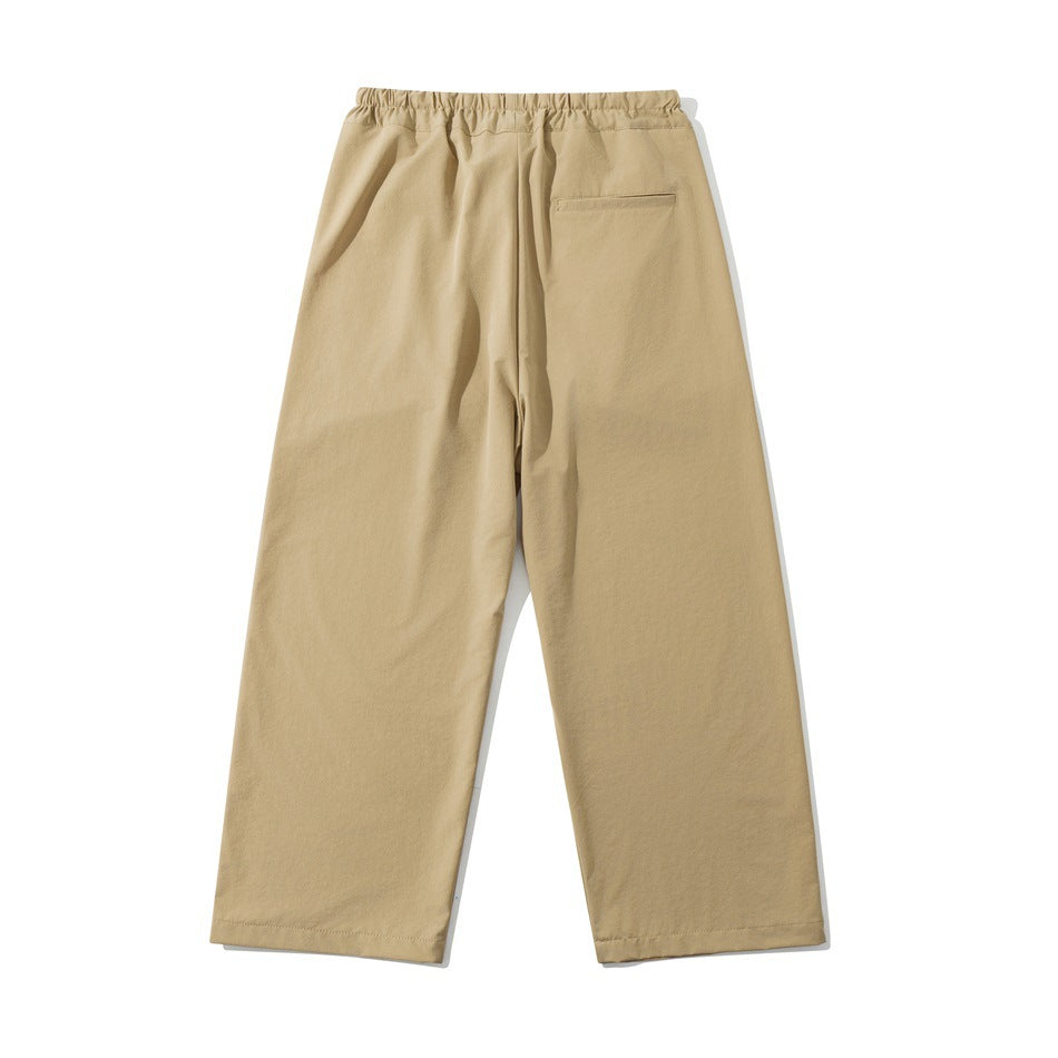 Back view of tan wide-leg trousers with an elastic waistband and one welt pocket.