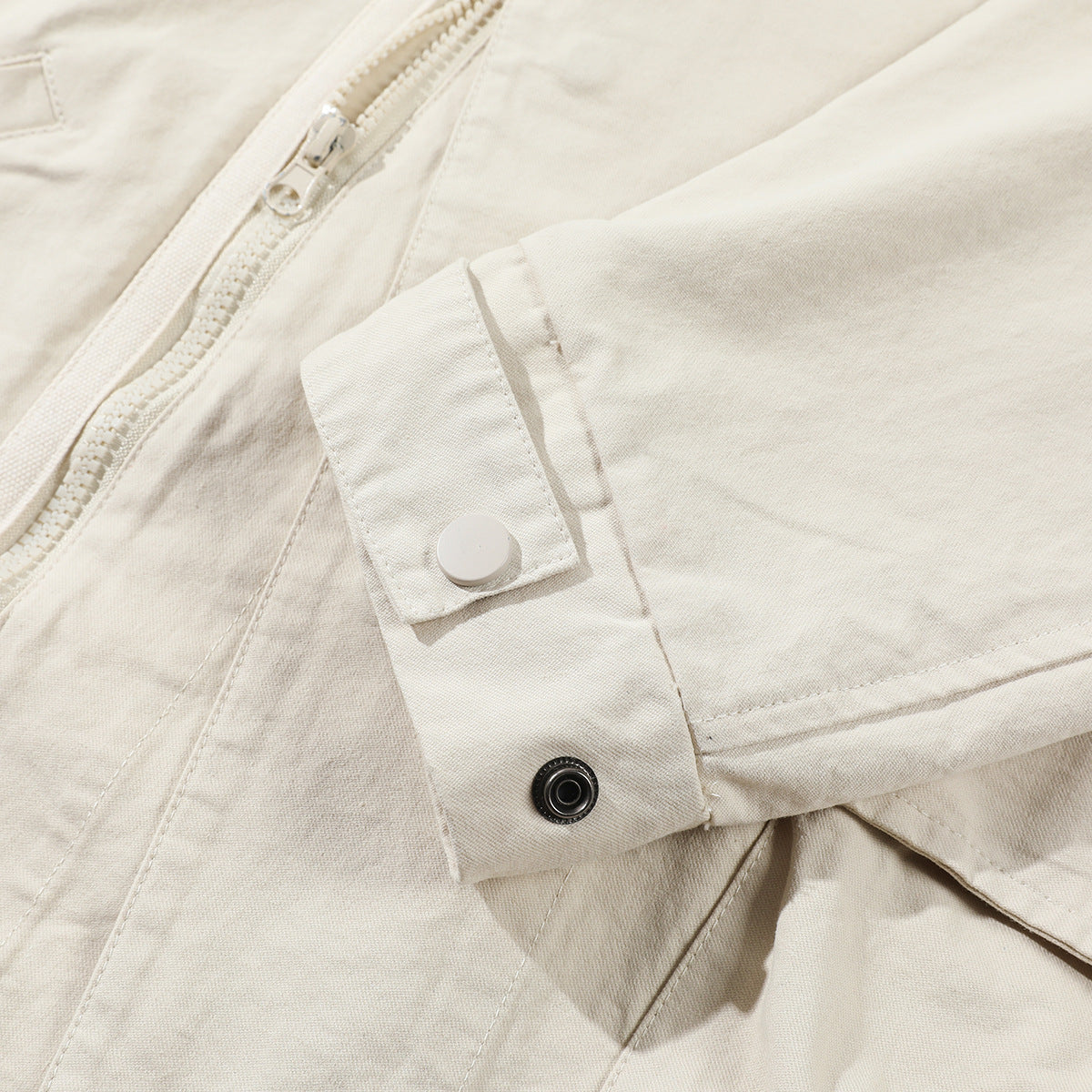 Close-up of an off-white jacket showing a zipper, cuff tab, and snap fasteners.