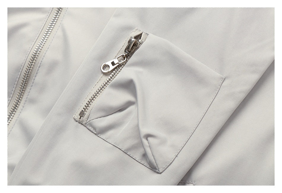Close-up of a light gray jacket with a silver zipper pocket and stitched flap.