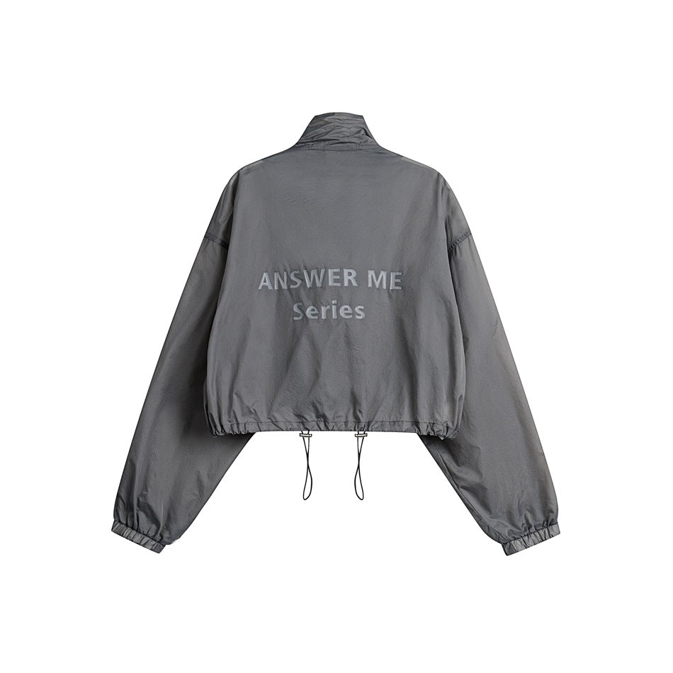 Back view of a gray cropped jacket with a high collar, elastic cuffs and hem, drawcords, and white “ANSWER ME Series”