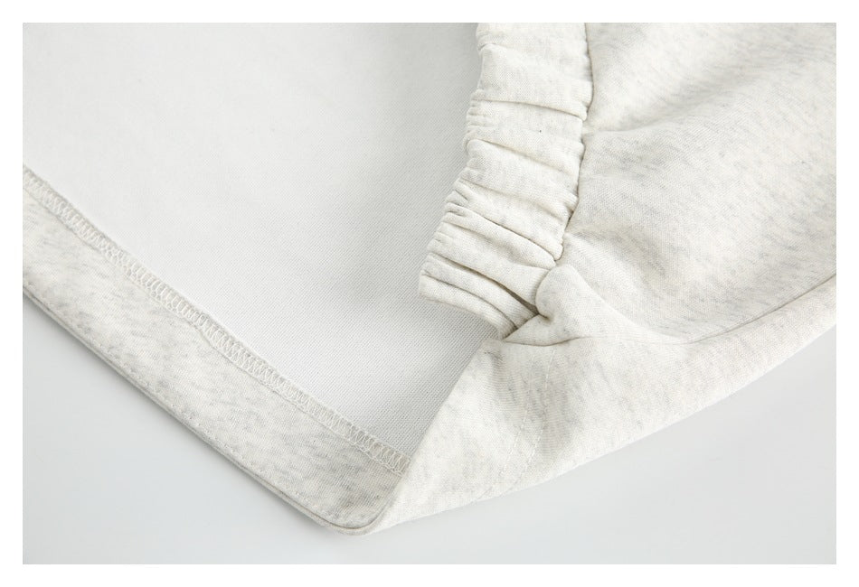 Close-up of an elasticized gathered edge and overlocked seam on light gray heather fabric.