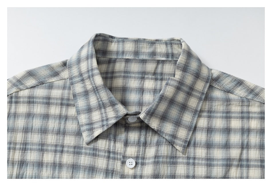 Close-up of the pointed collar and white button on a gray, blue, and cream plaid shirt.