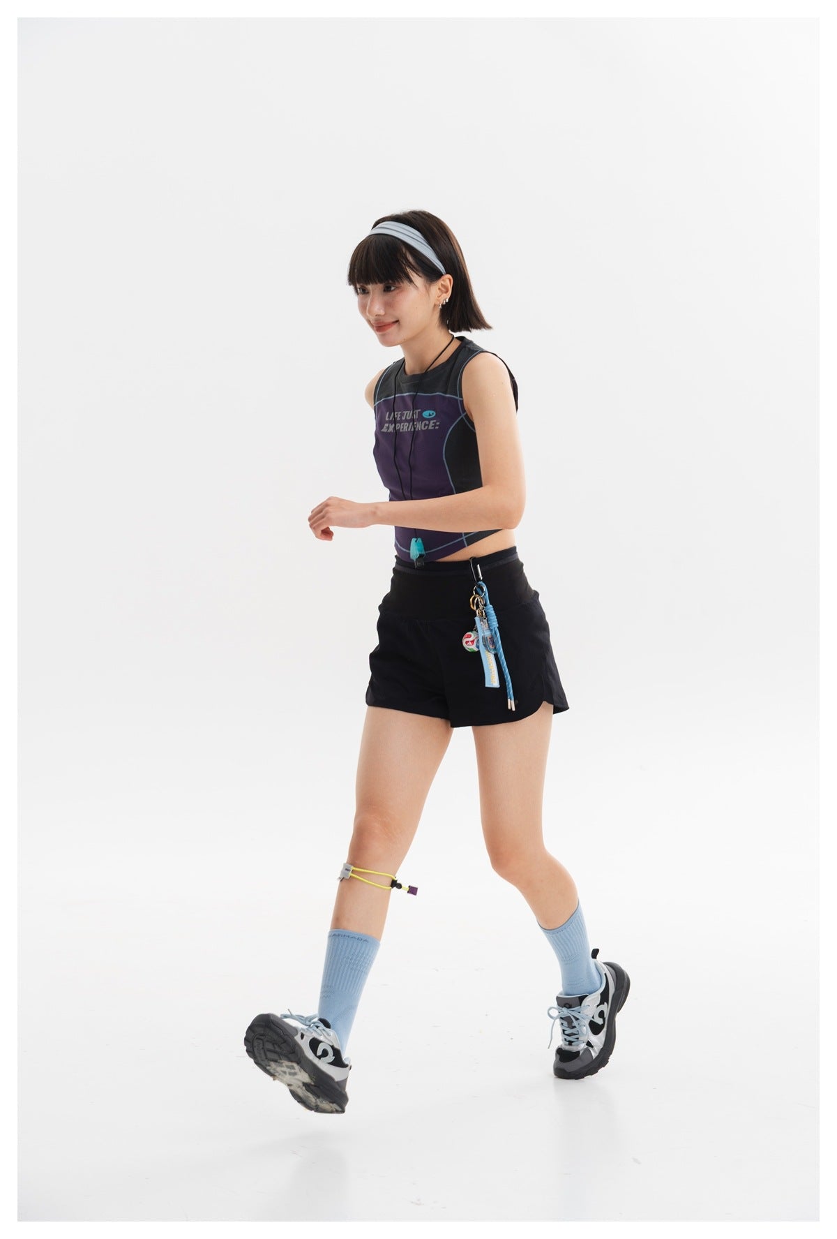 Model walking in a purple and charcoal sleeveless crop top with black shorts.