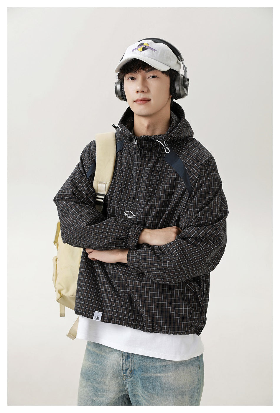 Model wearing a dark grid-plaid hooded pullover jacket, shown from the front with arms crossed.