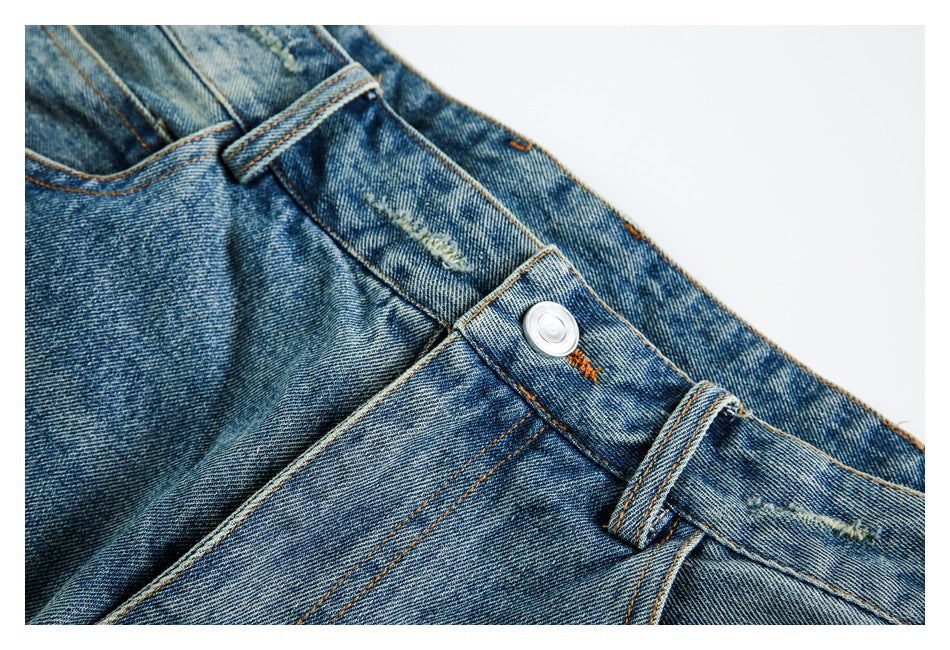 Close-up of blue washed jeans showing the waistband, belt loop, silver button and orange stitching.