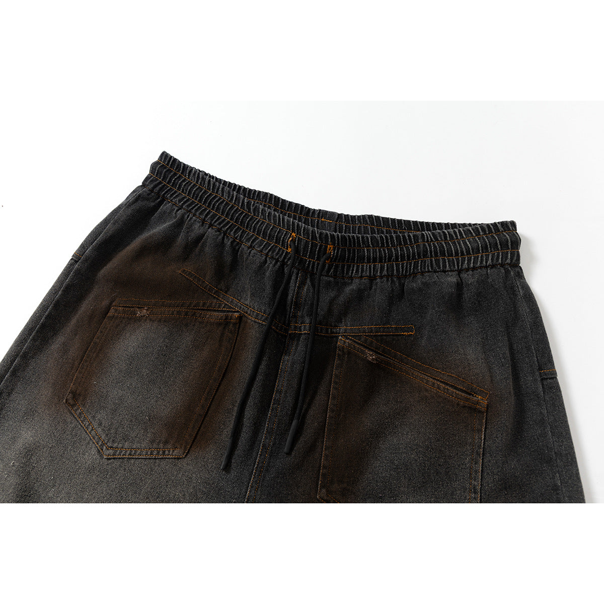 Close-up of charcoal-black washed shorts showing an elastic waistband, black drawstrings, and two rear patch pockets.