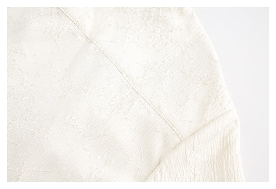 Close-up of ivory raised-pattern fabric showing a diagonal seam and gathered section.