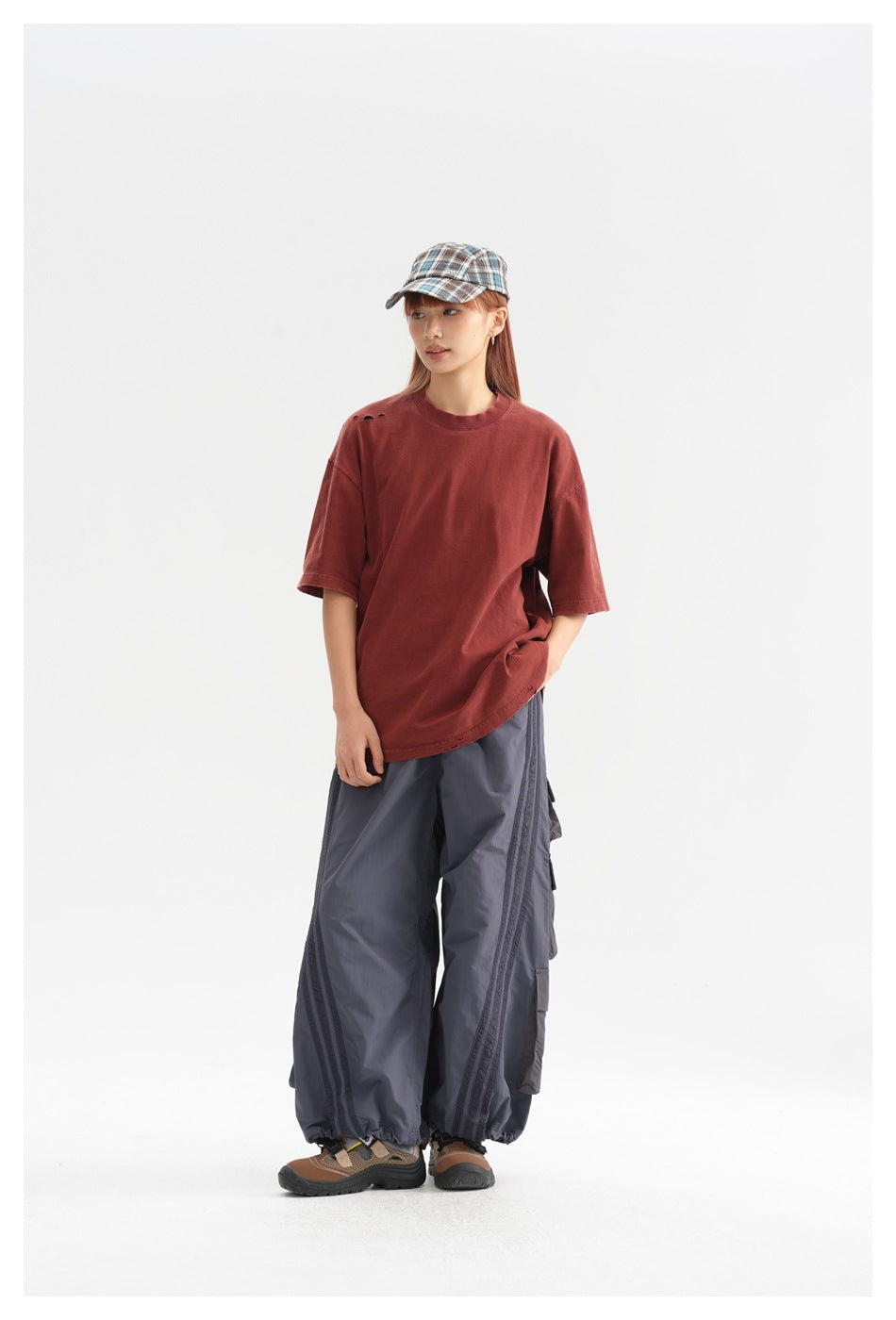 Model in a brick-red oversized T-shirt and gray cargo pants, posing with one hand in a pocket.