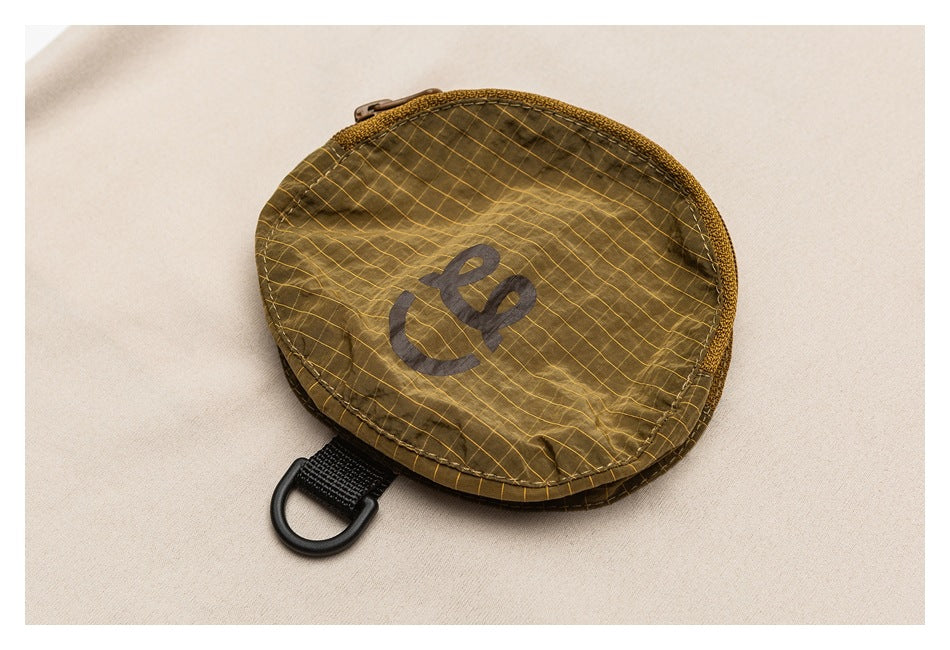 Close-up of a brown oval zip pouch with a yellow grid pattern and a black loop on beige fabric.