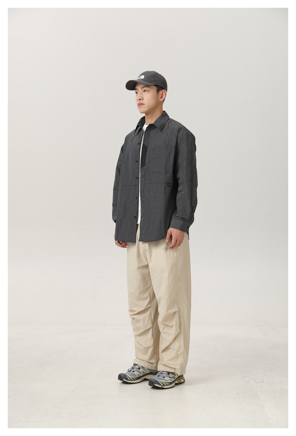 Model wearing the black and white check shirt open over a white tee with beige trousers, side view