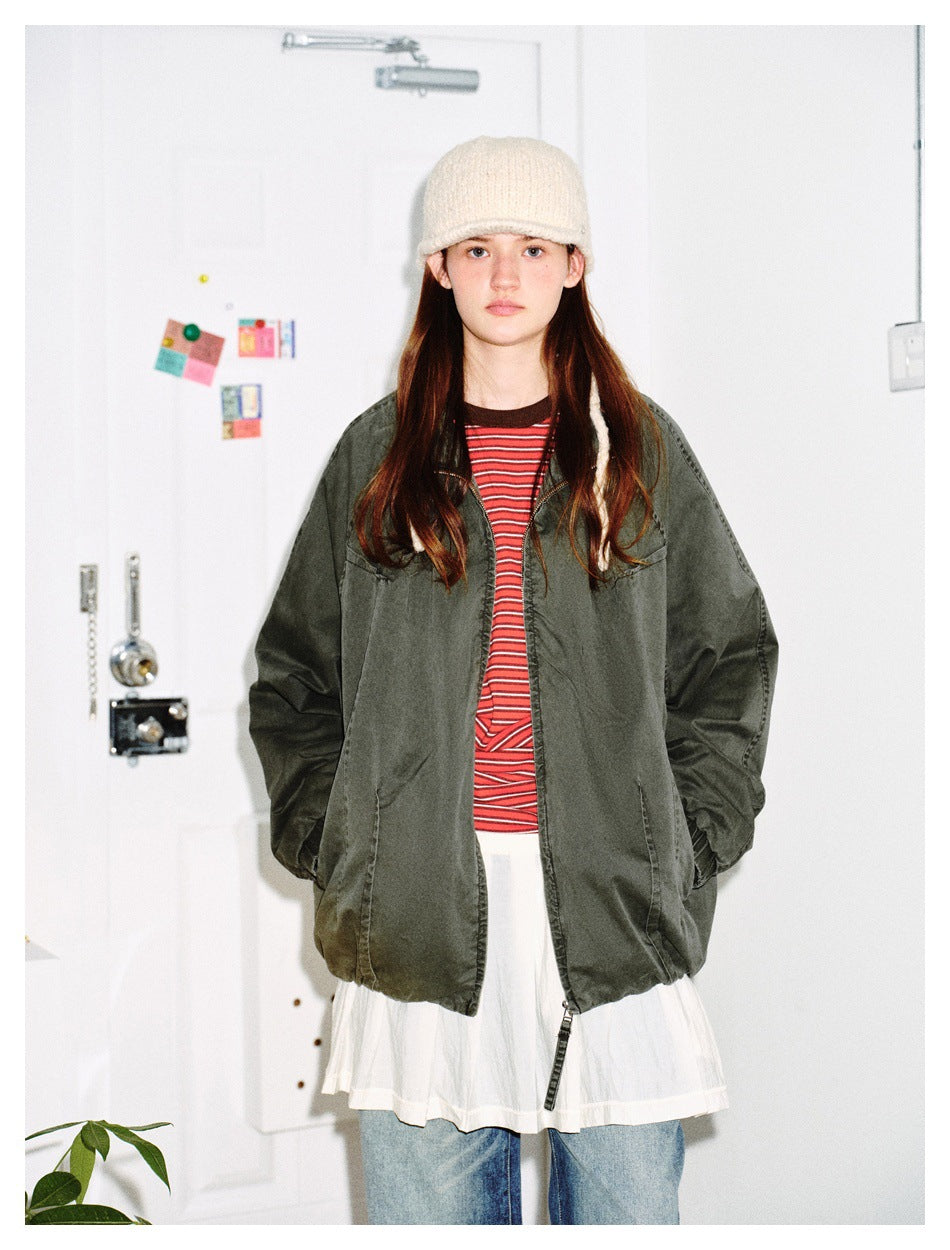 Model facing forward in an oversized green zip jacket worn open with hands in pockets over a striped tee and jeans