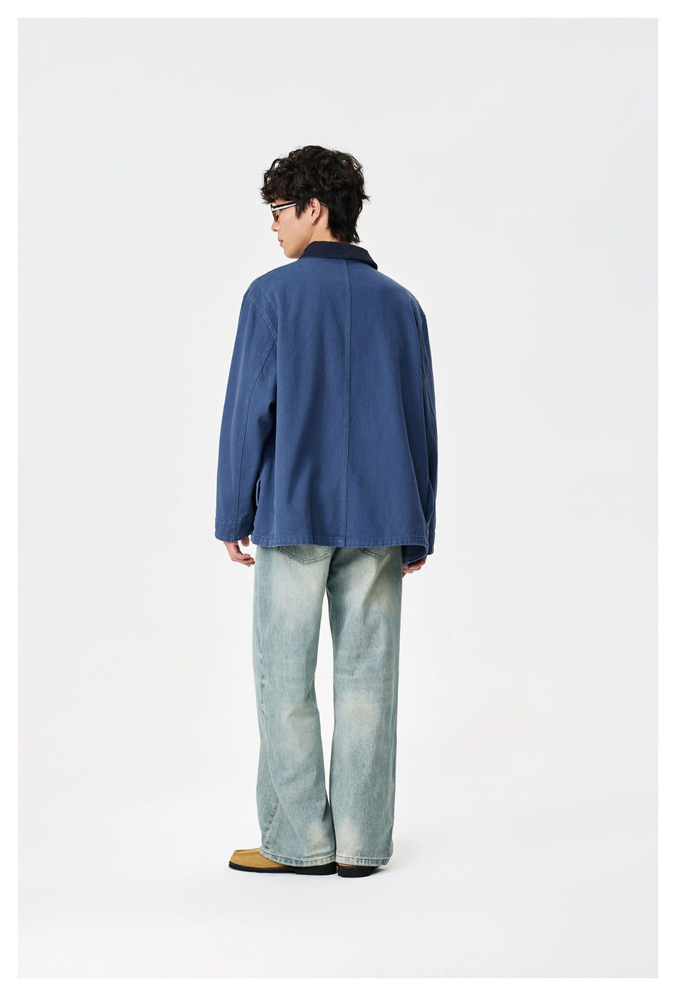 Model wearing the back of a blue work jacket with a dark contrast collar and light-wash wide-leg jeans.