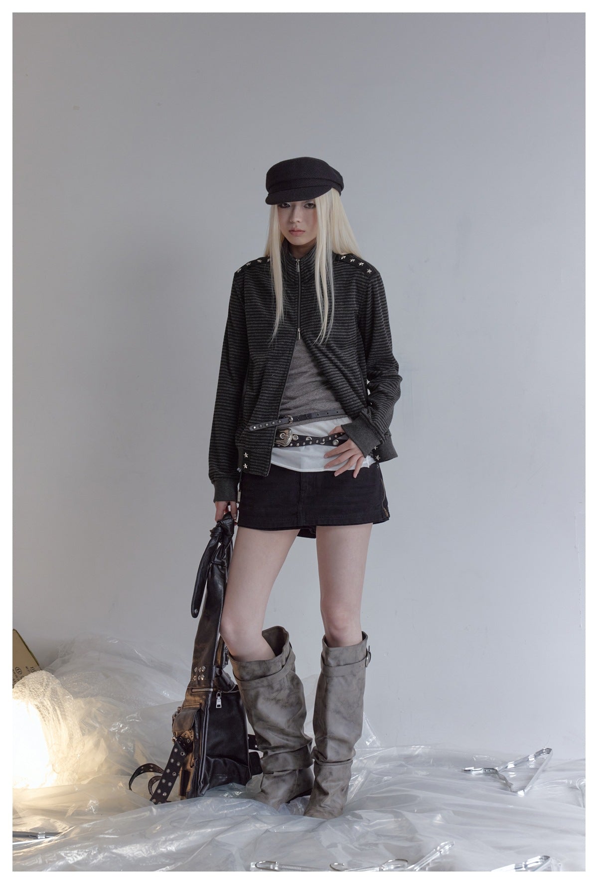 Model wearing the striped star-studded zip jacket open over a gray top with a black mini skirt and gray boots