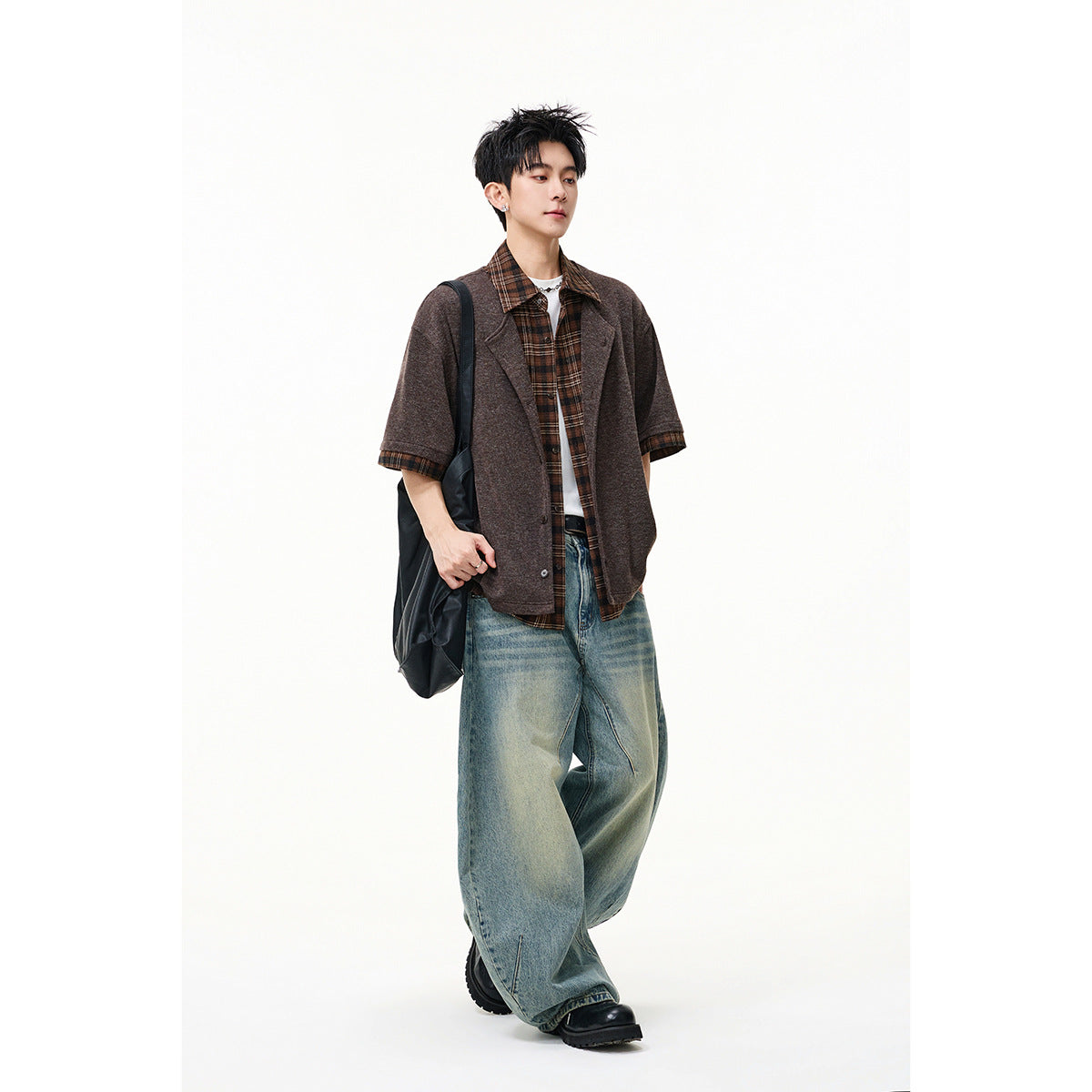 Model wearing a brown short-sleeve button-front overshirt layered over a brown plaid shirt, with loose blue jeans.