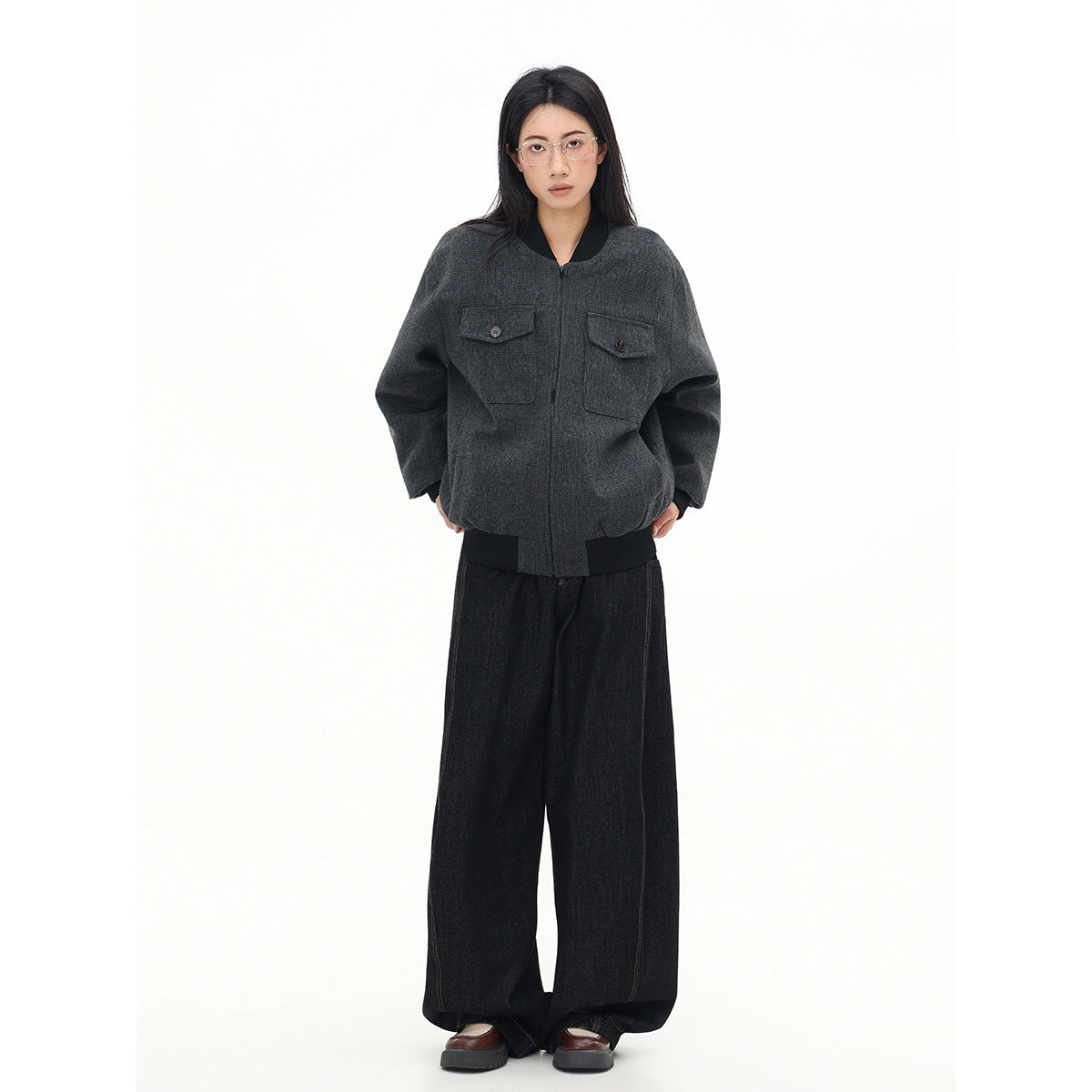 Full-length front view of a model wearing a charcoal plaid bomber jacket with black ribbed trim and flap chest pockets.