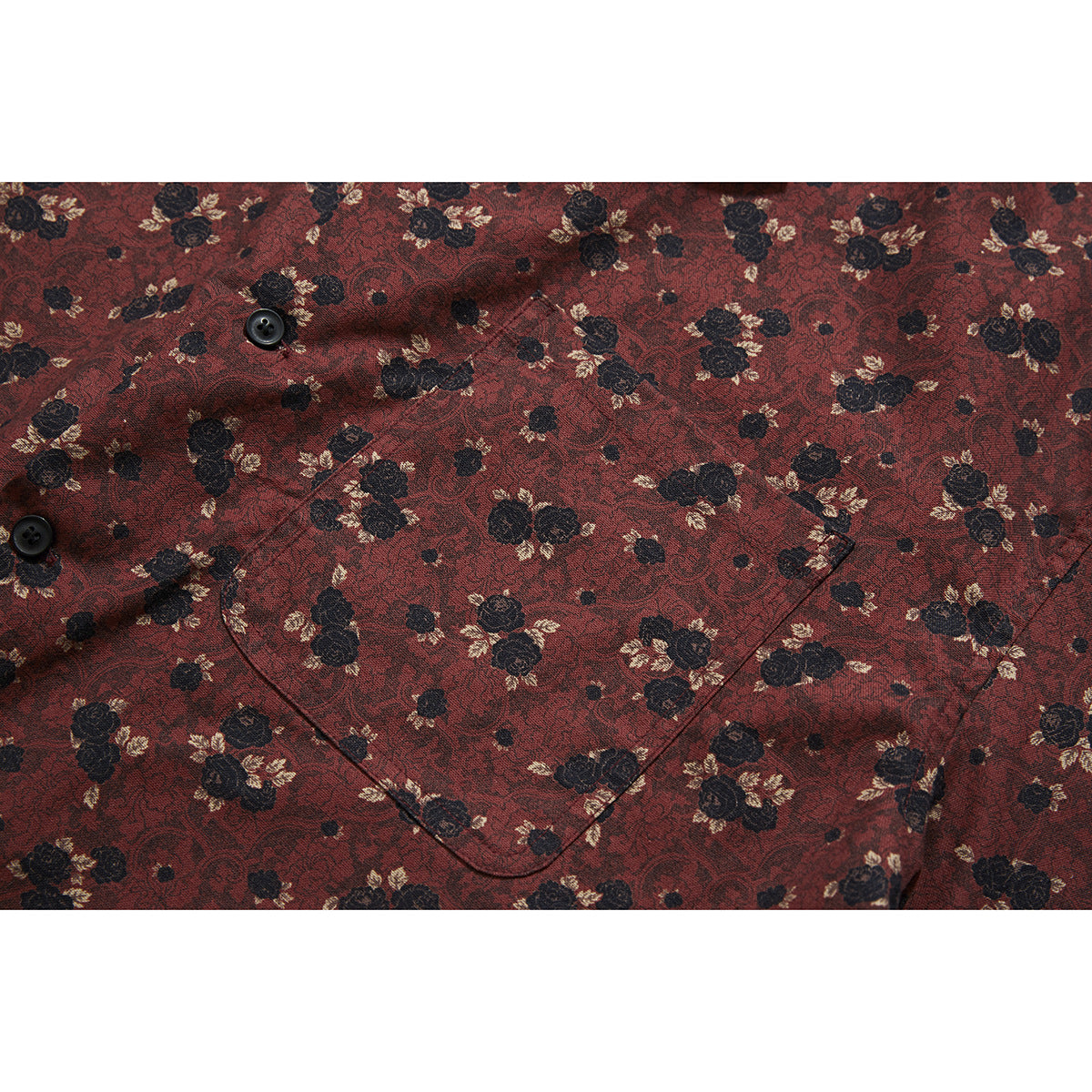 Close-up of a black button and patch pocket on a burgundy floral shirt.