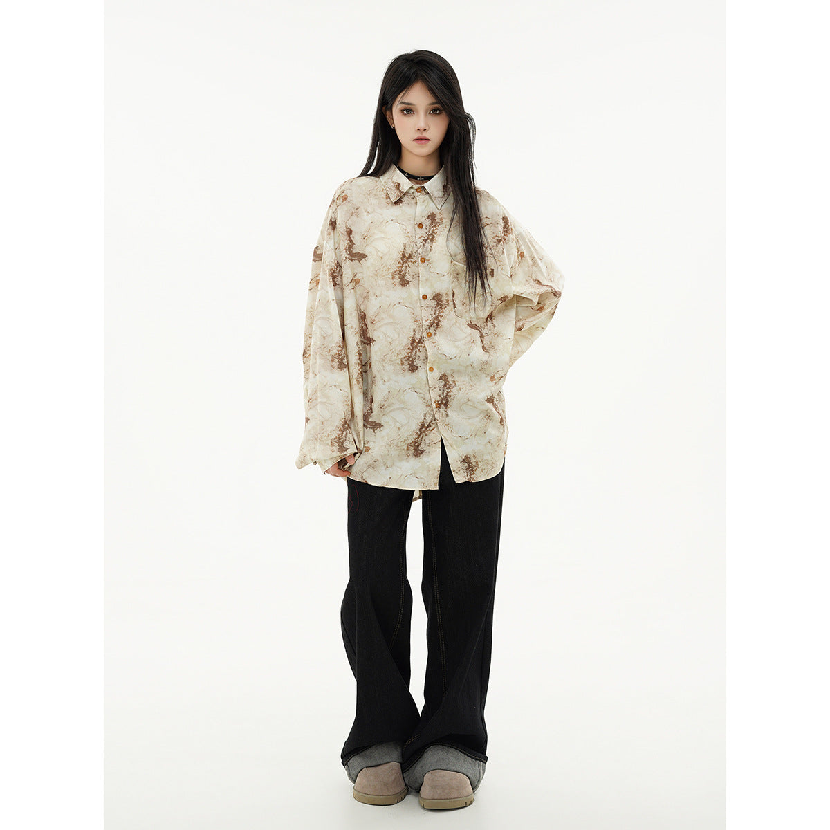 Front view of a model in an oversized cream and brown abstract-print button-up shirt, black wide-leg jeans, and taupe shoes.