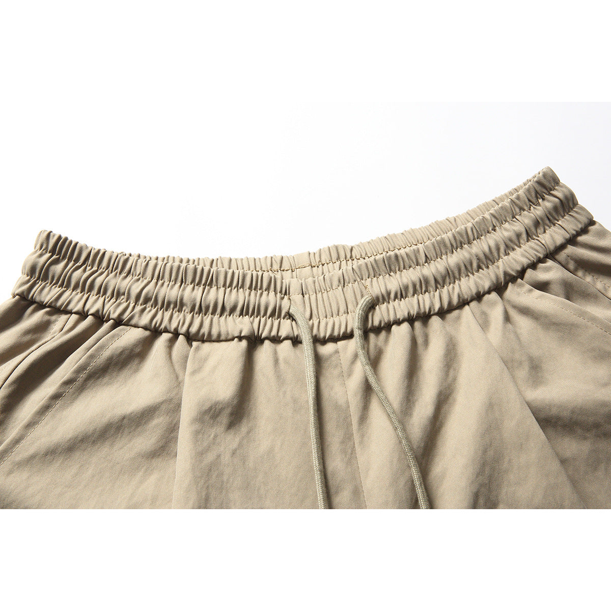 Close-up of beige shorts with a gathered elastic waistband and matching drawstrings.