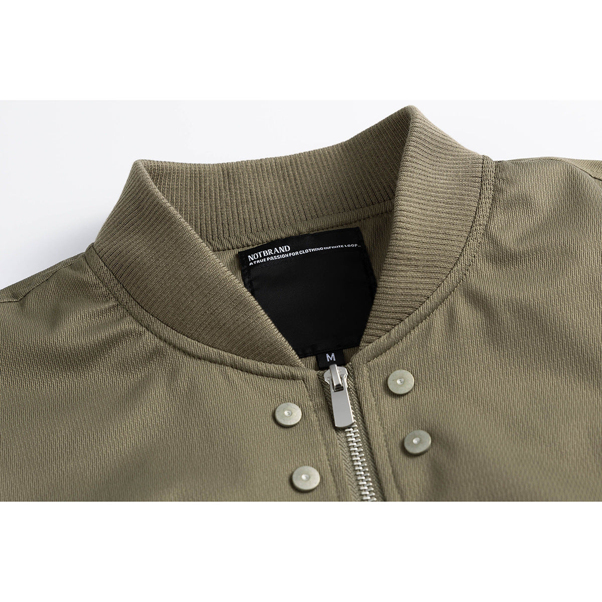 Close-up of an olive jacket’s ribbed collar, zipper, metal snaps and black inner label.