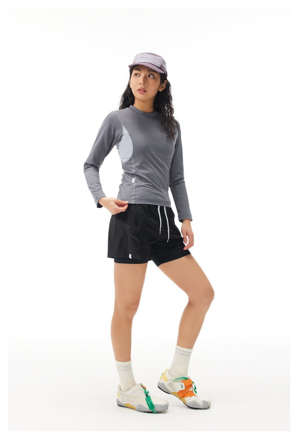 Model wearing a gray long-sleeve top with pale mesh side panels and black shorts, shown from the front at an angle.