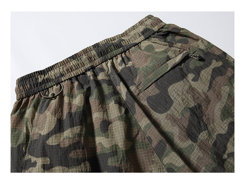 Close-up front view of olive, brown and black camouflage pants with an elastic waistband and a flap pocket.